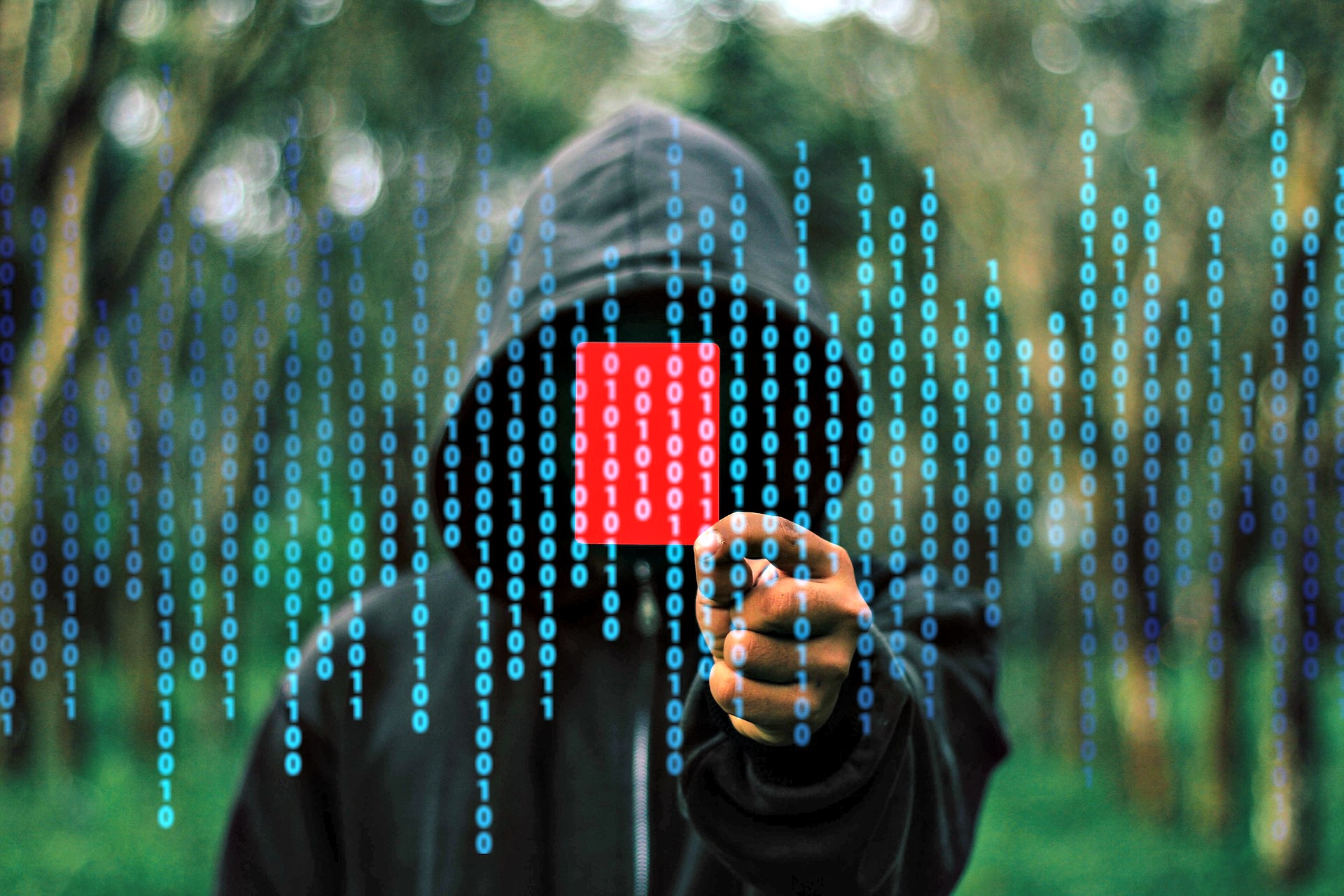 A hooded man (hacker) pointing at the camera with 0s and 1s